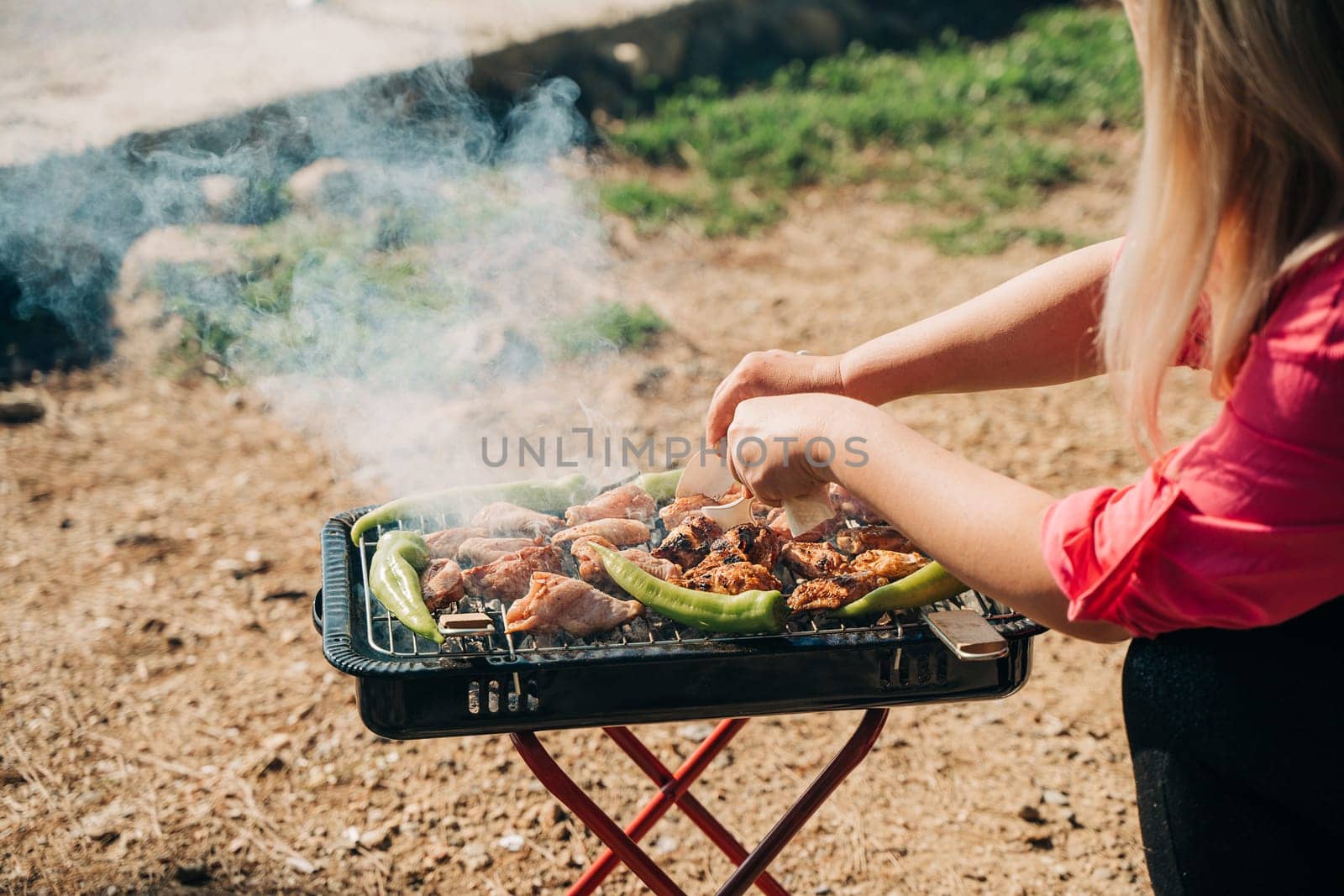 Barbecue grill with chicken, meat, tomatoes and green pepper in nature forest camping park with sea on background. Woman cooking outdoors