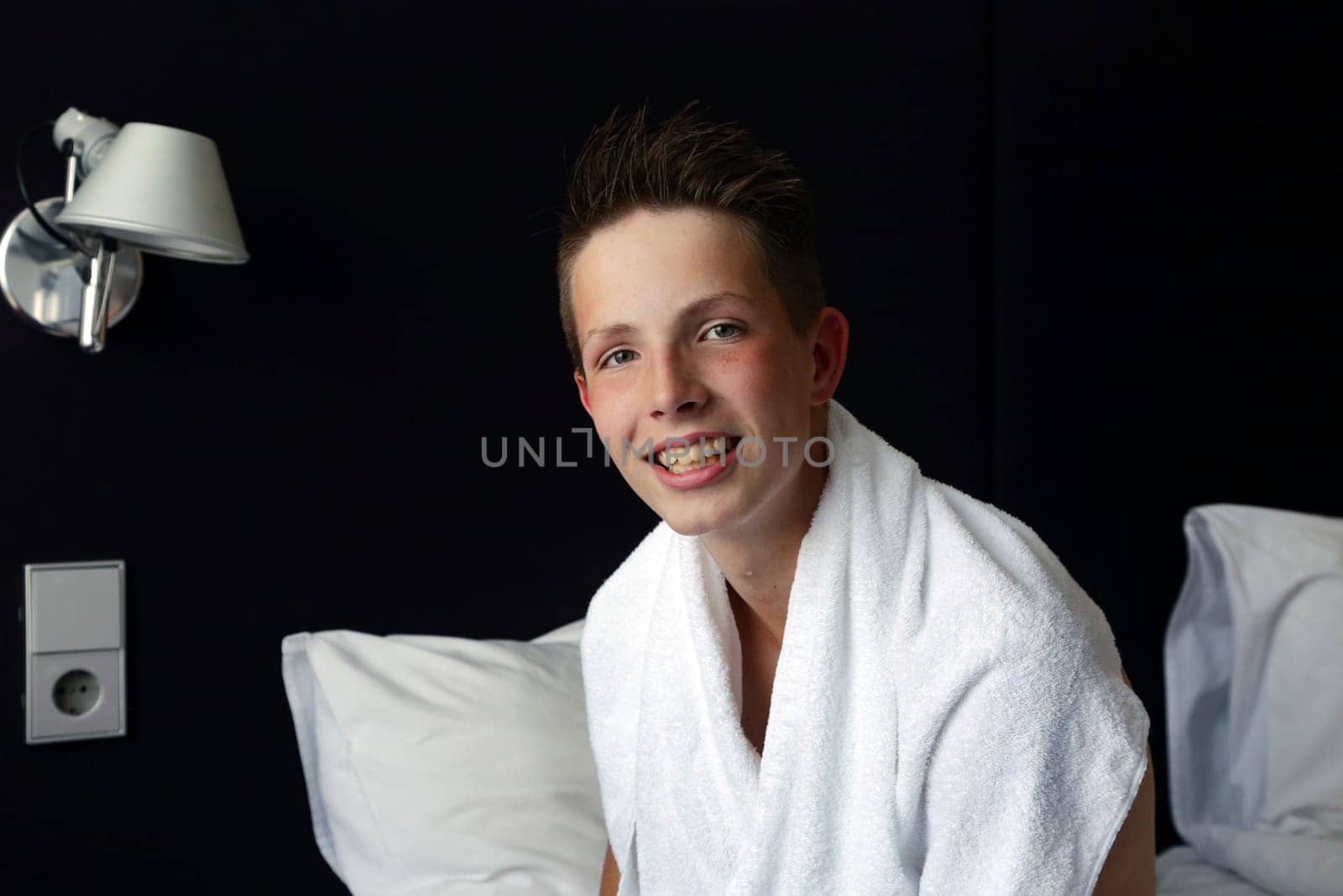 A cute teenage boy with a white towel draped over himself. High quality photoBeauty portrait of a young man in a home bathroom with a white towel around his neck, joyful and looking at camera, interior.