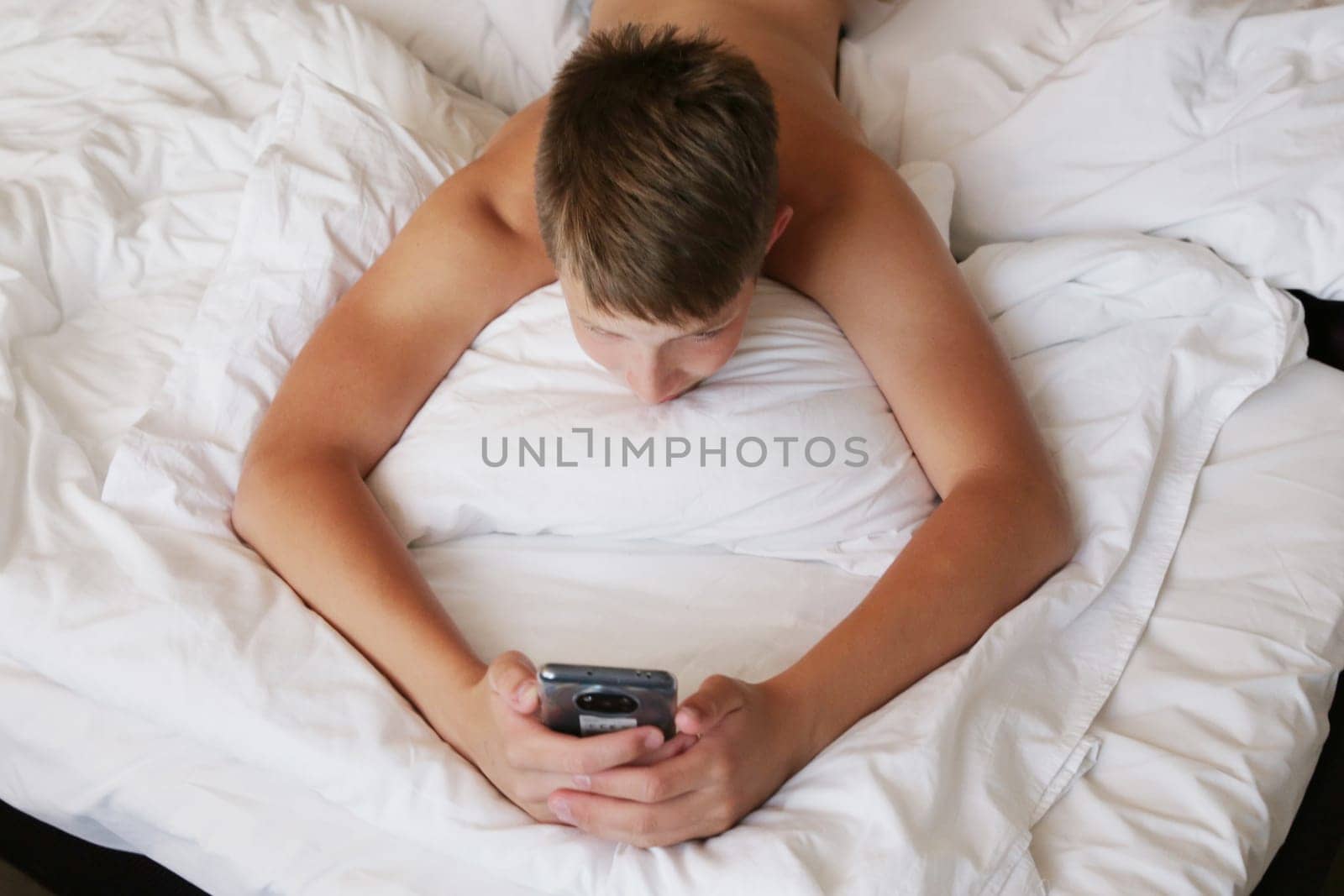The boy lies on the bed with the phone. by gelog67