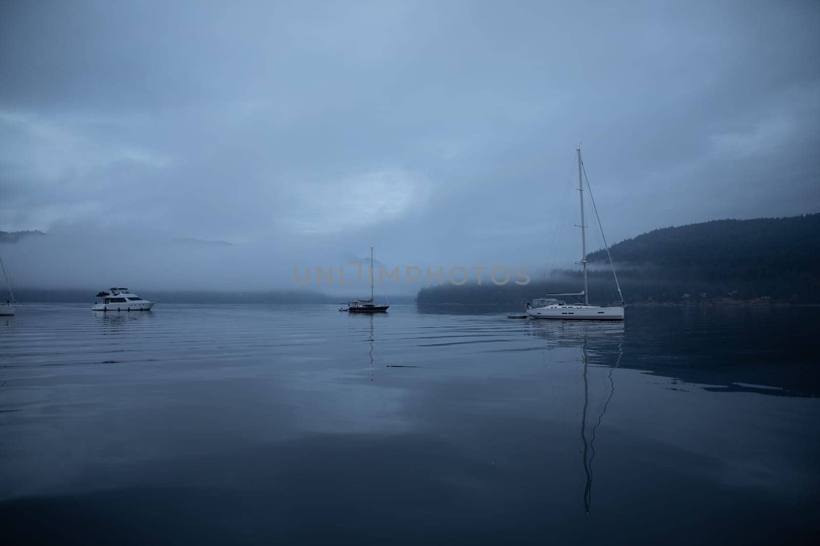 Boats anchored in a cove under dark and moody skies by Granchinho
