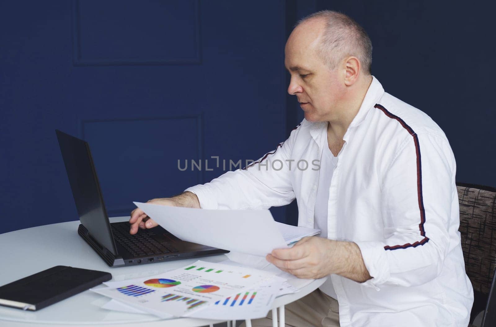 A male businessman works on a laptop, studies reporting documents, charts and graphs.