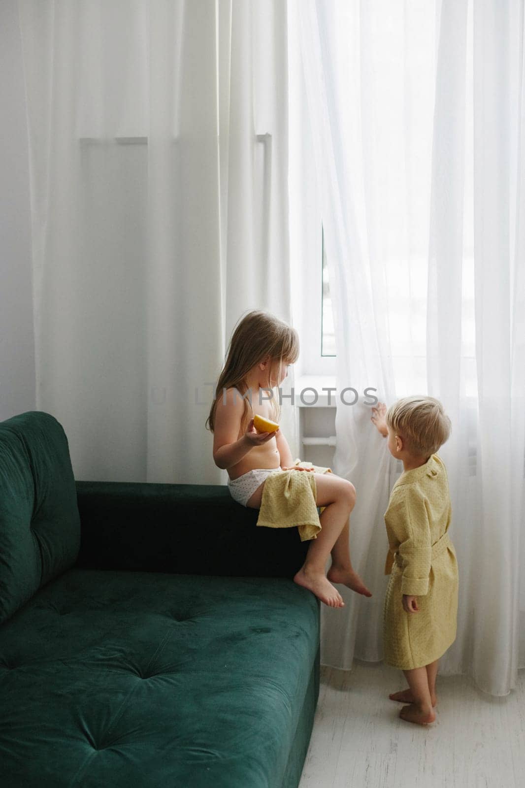 Children, a boy and a girl are resting after a bath, the girl is eating an orange.