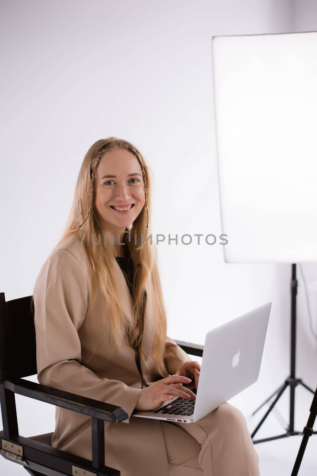A business woman in a suit is working, typing on a laptop apple and sitting on a producer chair. portrait blonde assistant of hands with computer MacBook . Vertical