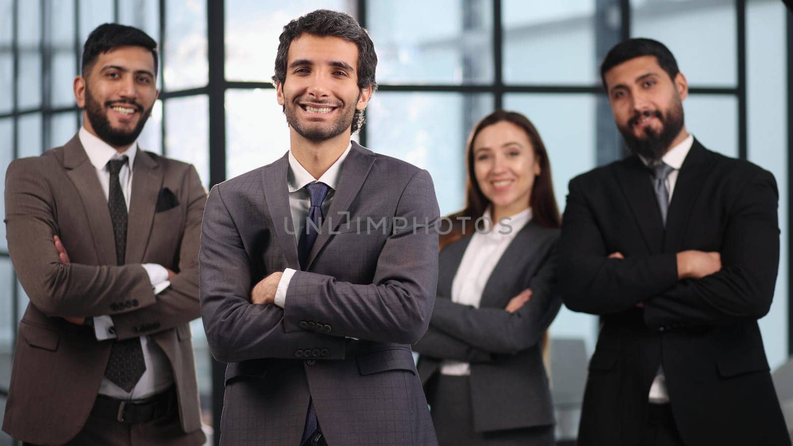 Attractive male leader standing with arms crossed in front of male executive team meeting