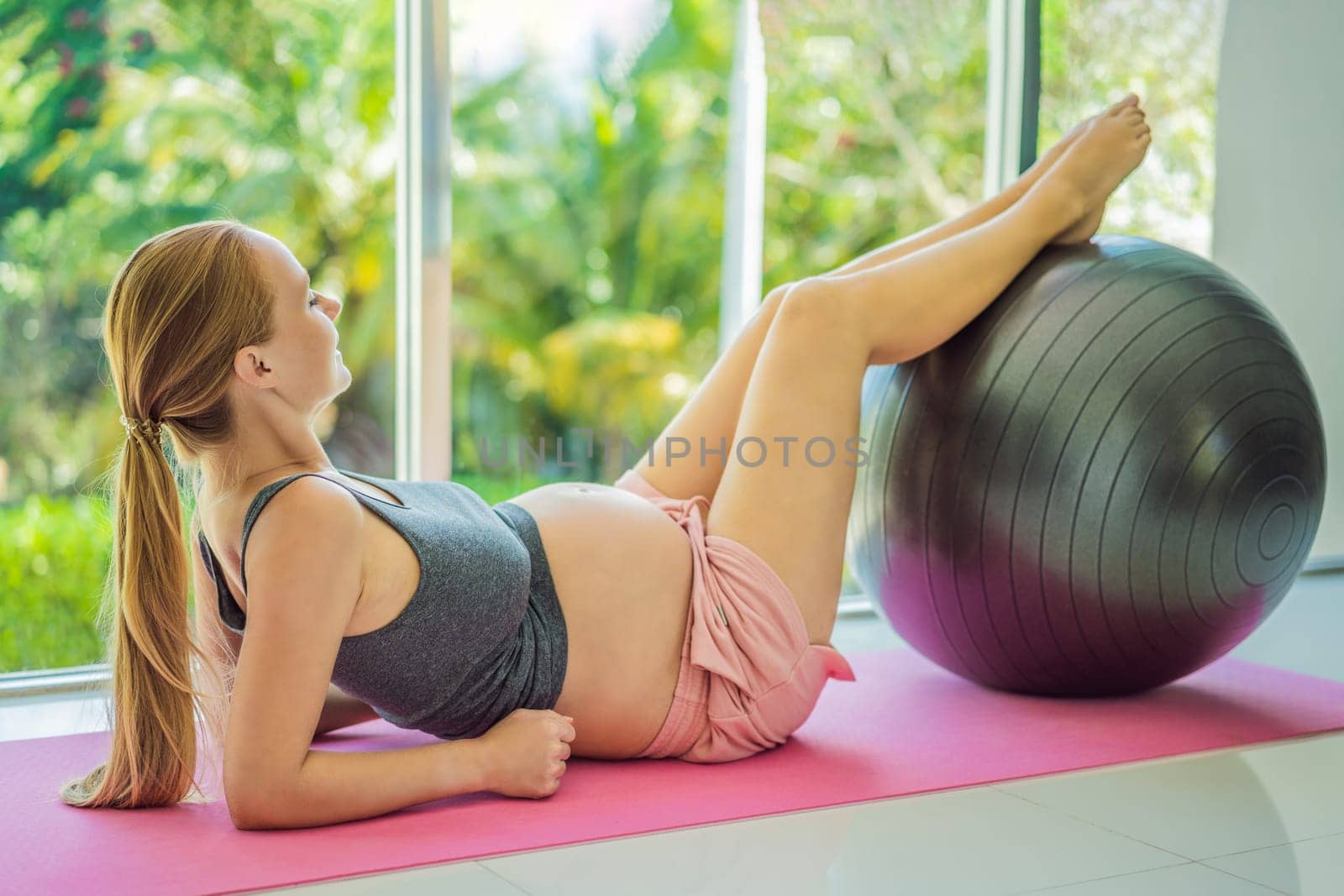 Pregnant woman exercising on fitball at home. Pregnant woman doing relax exercises with a fitness pilates ball. Against the background of the window.