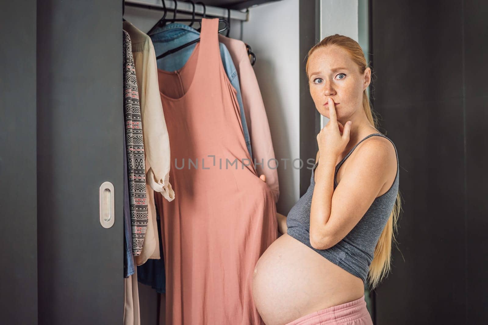A pregnant woman has nothing to wear. A pregnant woman stands in front of a closet with clothes and does not know what to wear because the clothes do not fit on her.