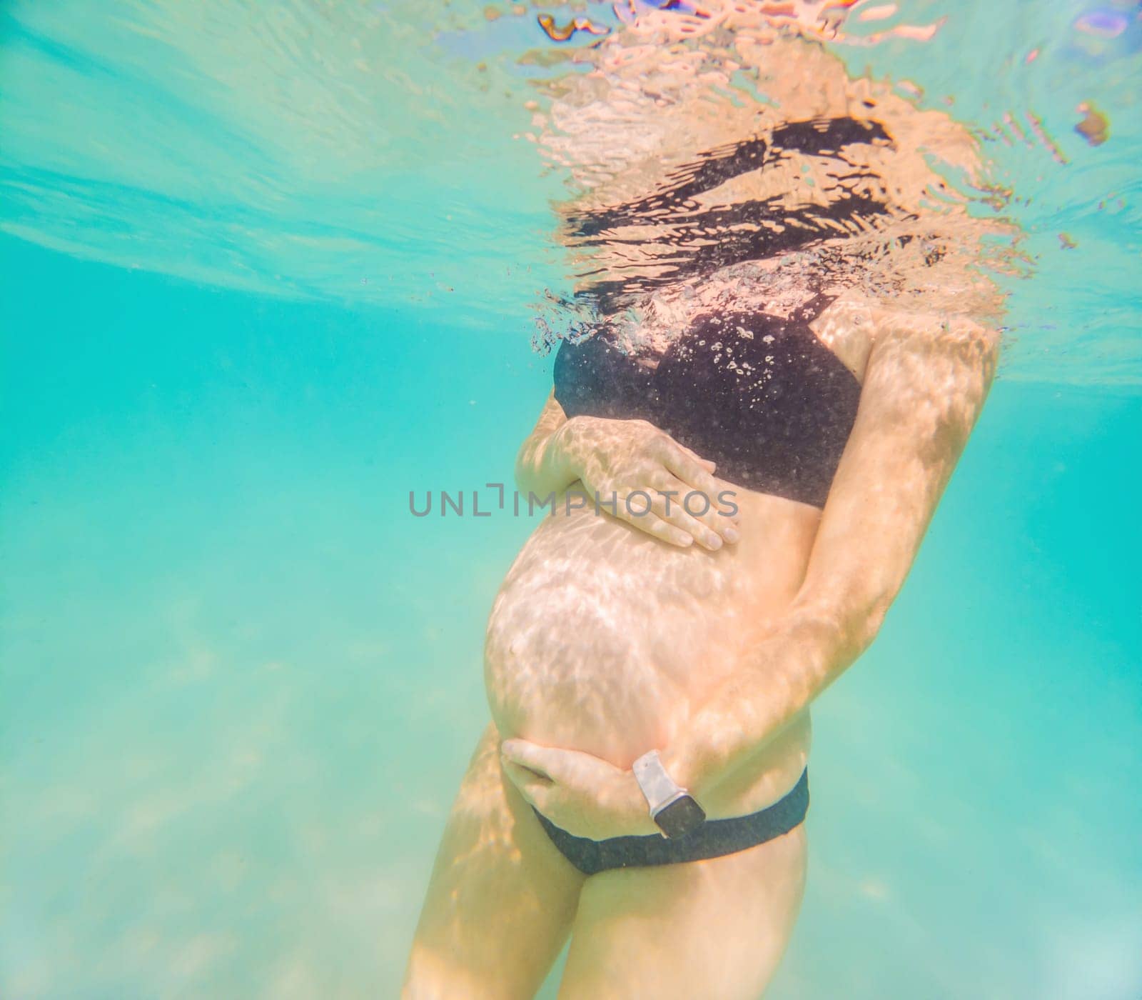 Pregnant woman underwater swimming in tropical sea. Healthy and active pregnancy. Young expecting mom on summer beach vacation before baby birth. Swim holiday and water fun. Travel during pregnancy. Underwater photography.