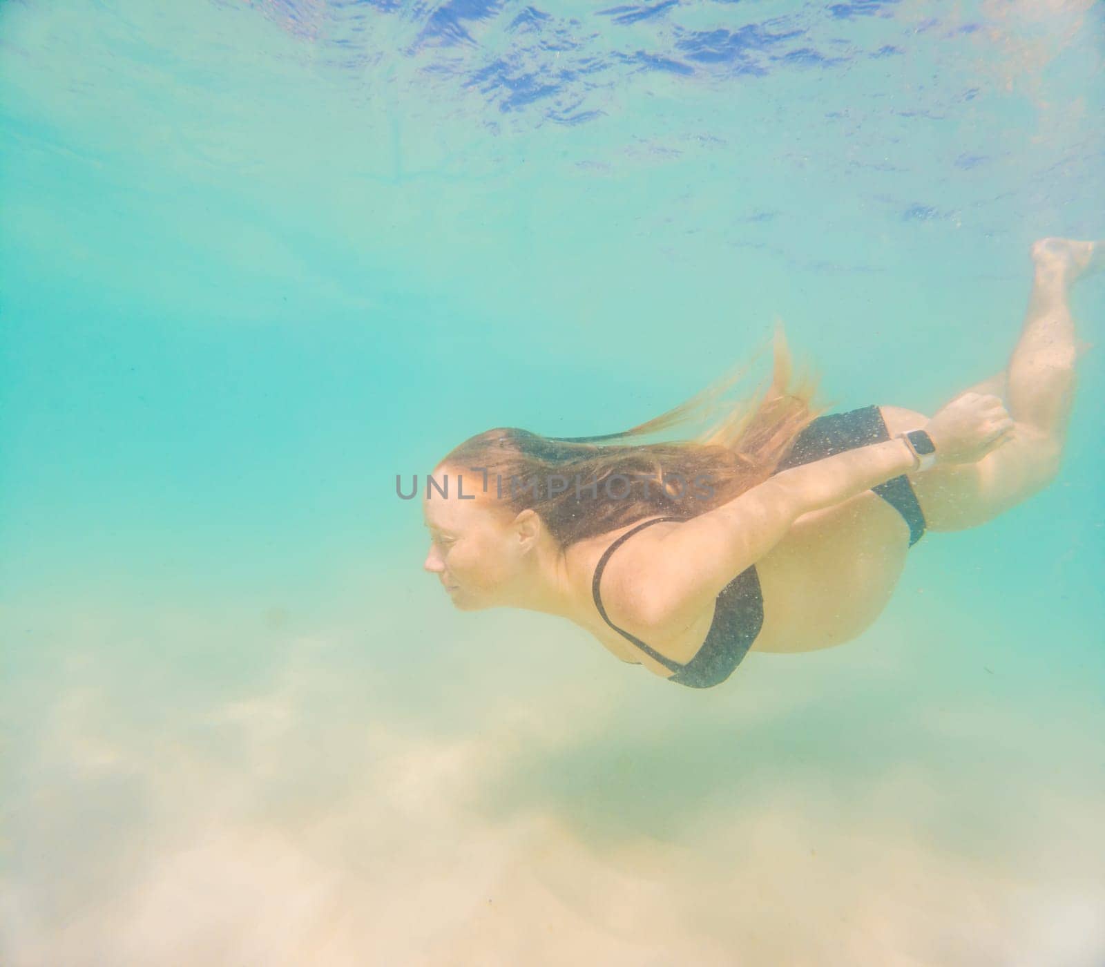 Pregnant woman underwater swimming in tropical sea. Healthy and active pregnancy. Young expecting mom on summer beach vacation before baby birth. Swim holiday and water fun. Travel during pregnancy. Underwater photography.