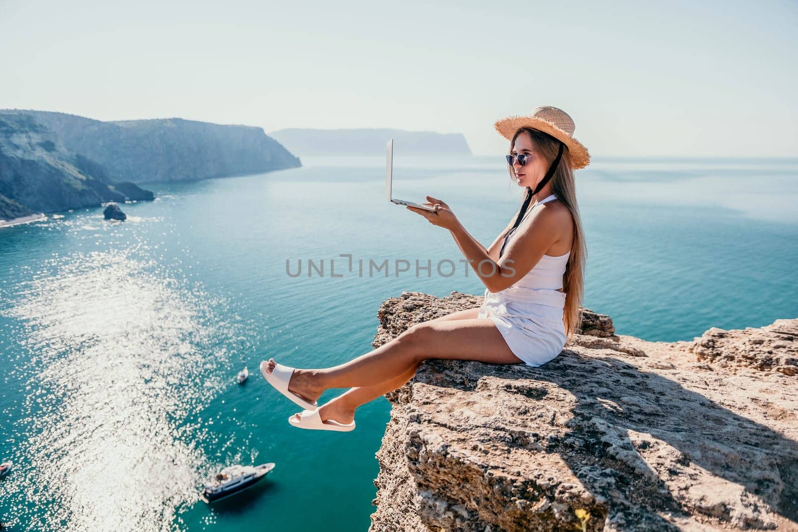 Digital nomad, Business woman working on laptop by the sea. Pretty lady typing on computer by the sea at sunset, makes a business transaction online from a distance. Freelance, remote work on vacation