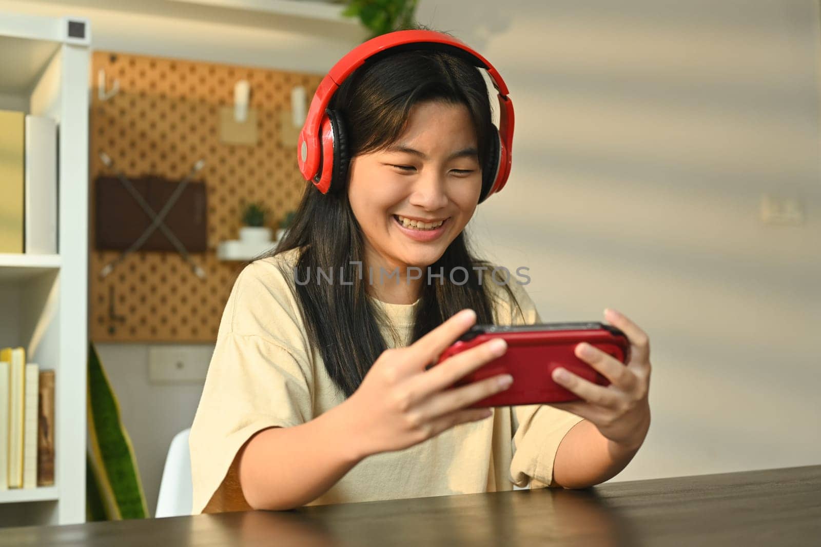 Joyful teenage asian girl playing video game on a portable game console at home. Leisure, entertainment and technology.