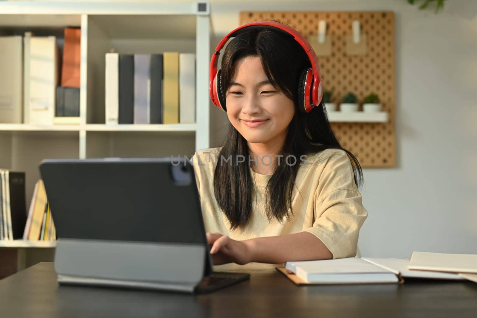 Happy asian girl wearing headphones sitting at table learning online at virtual class on laptop. Distance education concept by prathanchorruangsak