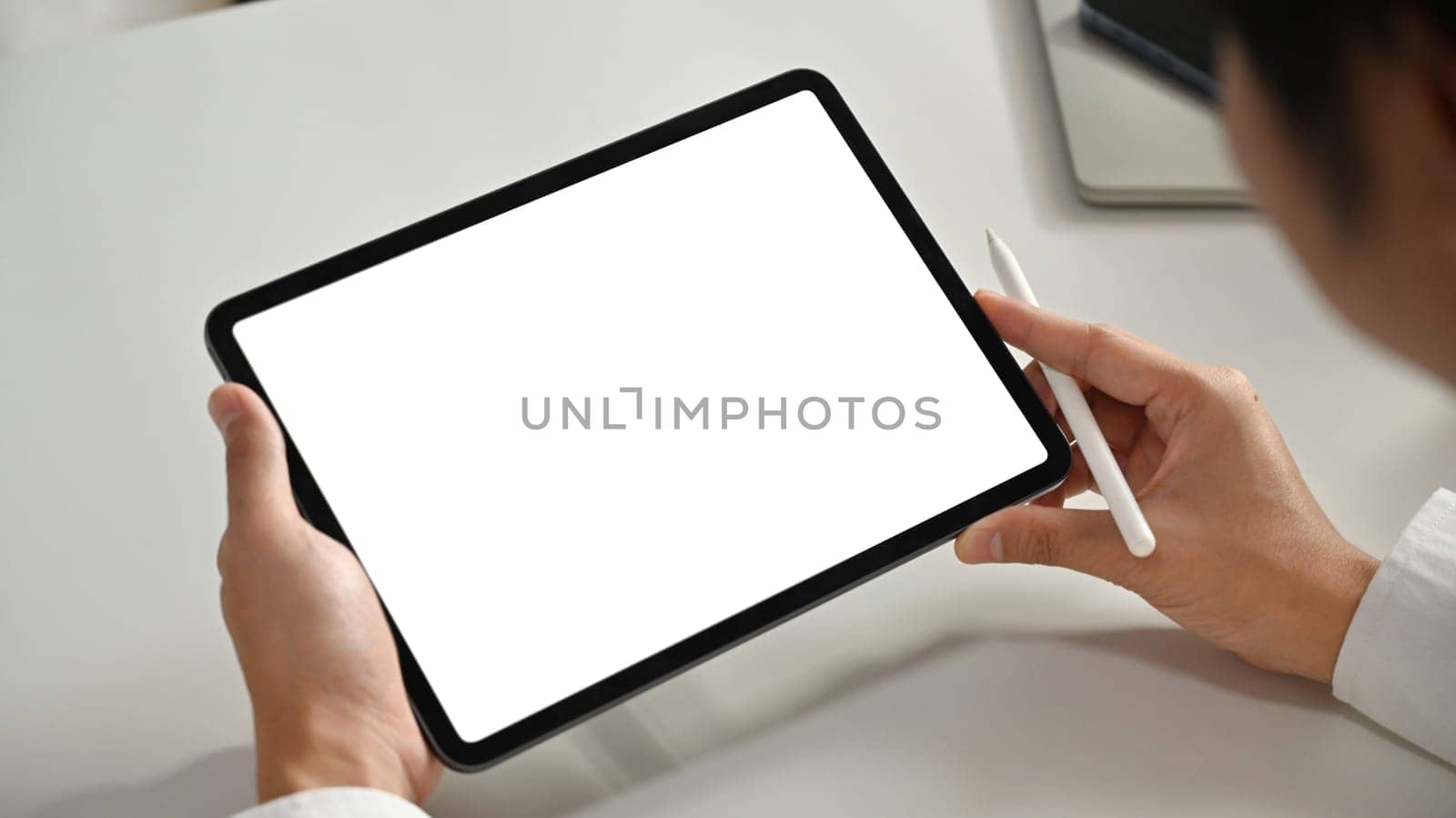 Close up view of young businessman hands holding stylus pen and using digital tablet at working desk. Empty screen for your text.