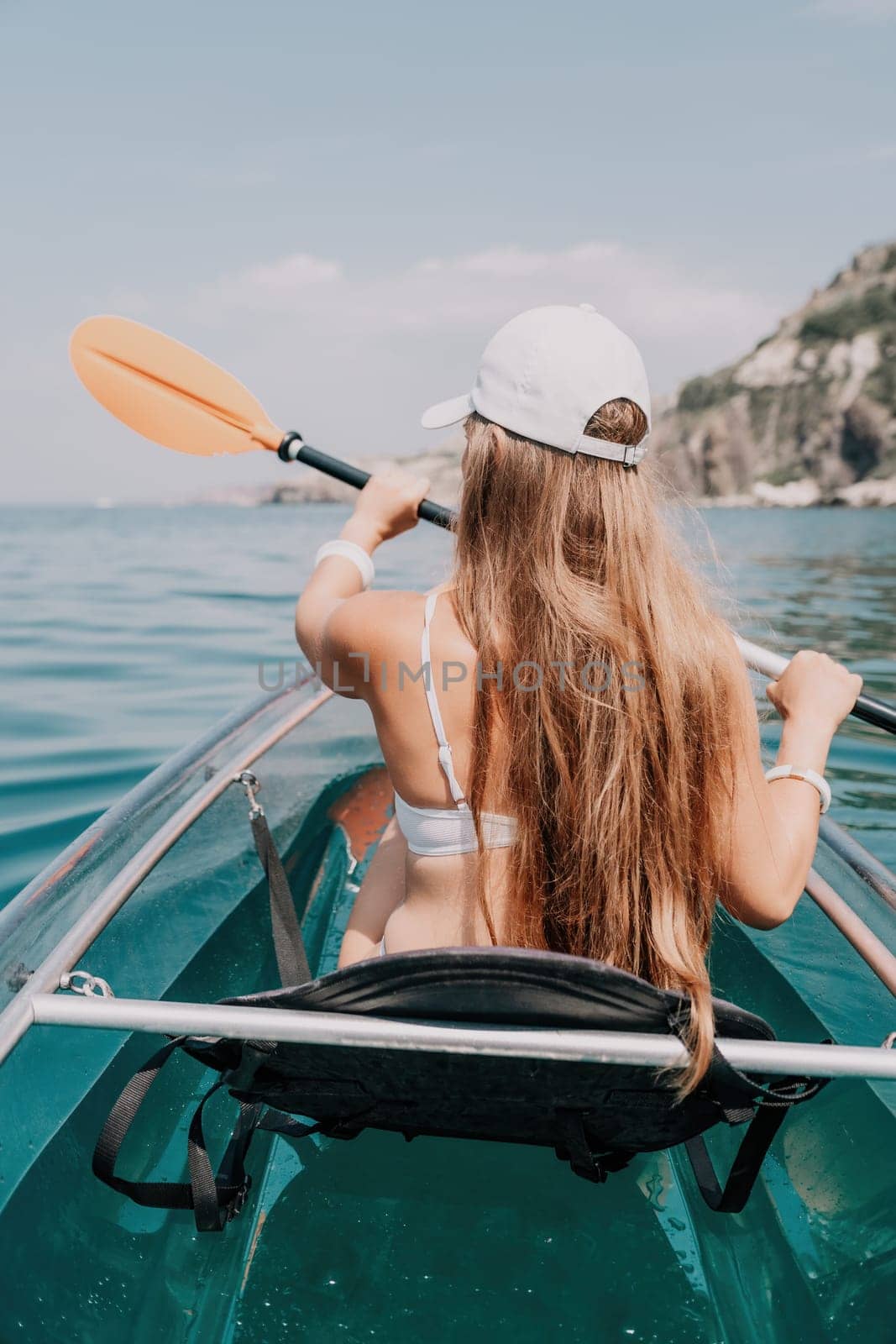 Woman in kayak back view. Happy young woman with long hair floating in transparent kayak on the crystal clear sea. Summer holiday vacation and cheerful female people having fun on the boat.