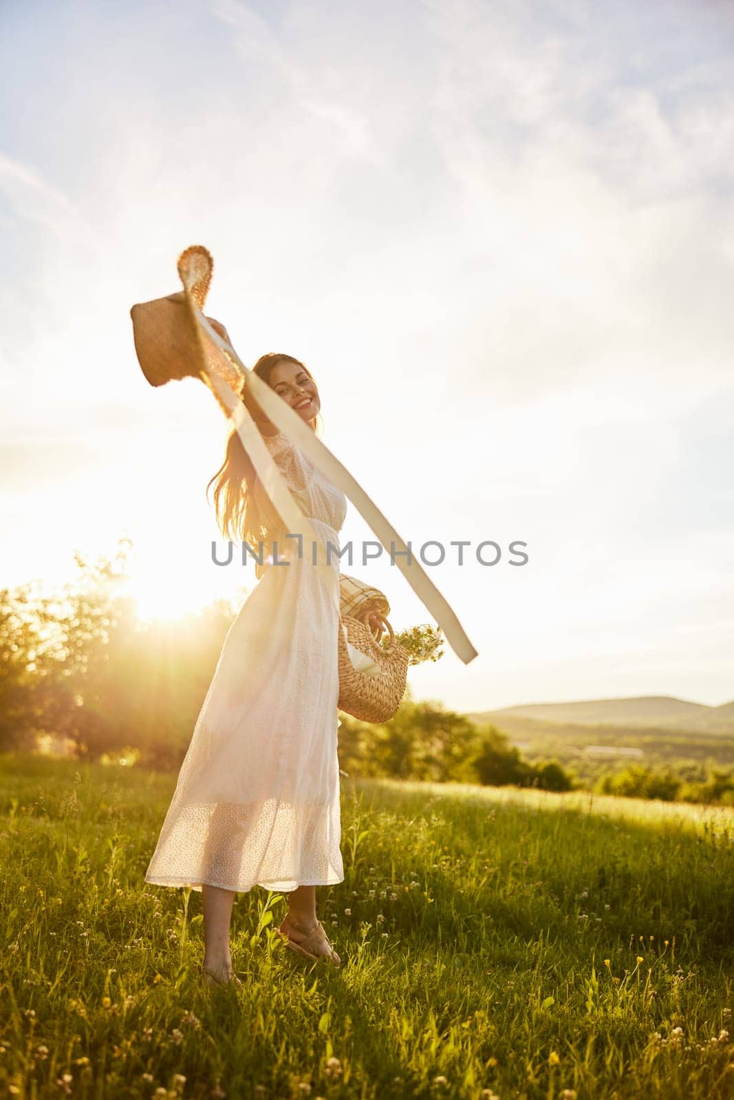 a woman in a light dress is happily spinning in nature, holding a hat in her hands, illuminated from the back by the sun. High quality photo