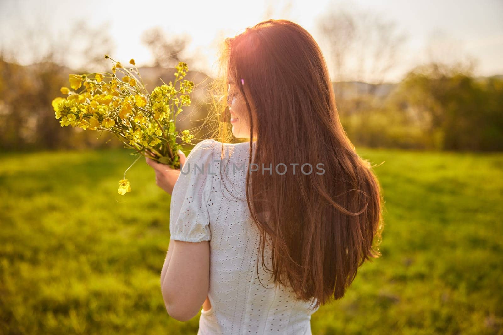 photo from the back of a red-haired woman with a bouquet of flowers in the rays of the setting sun. High quality photo