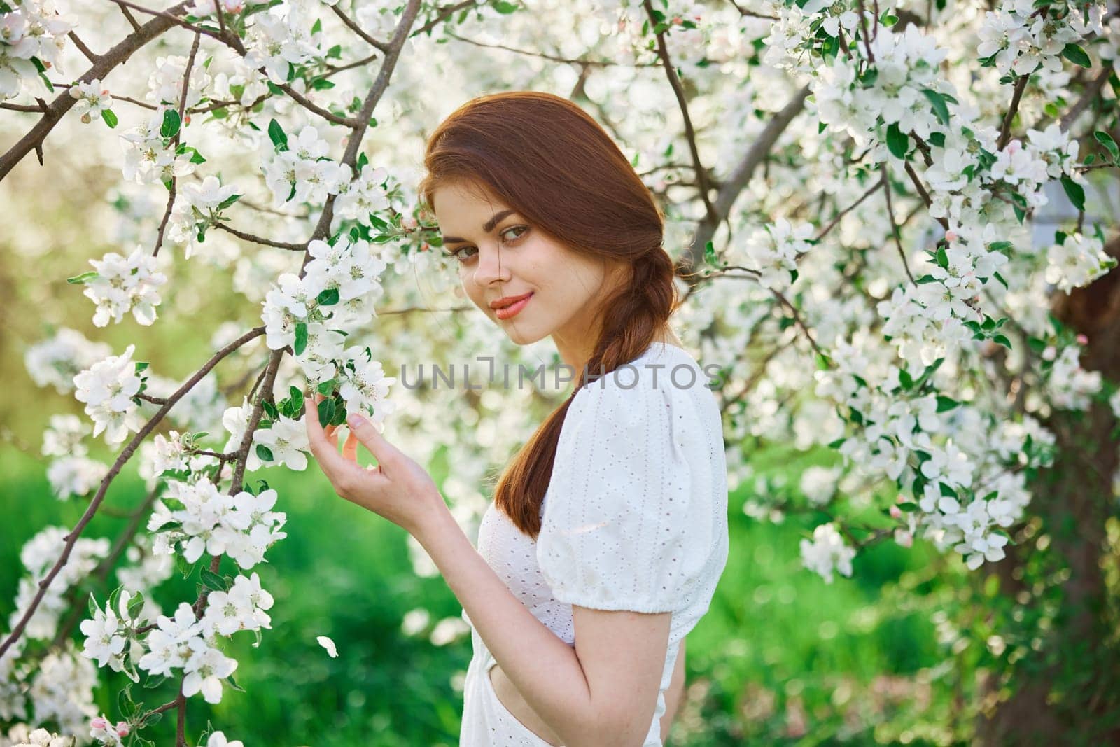 a beautiful woman in a light dress enjoys the spring while standing next to a flowering tree. High quality photo