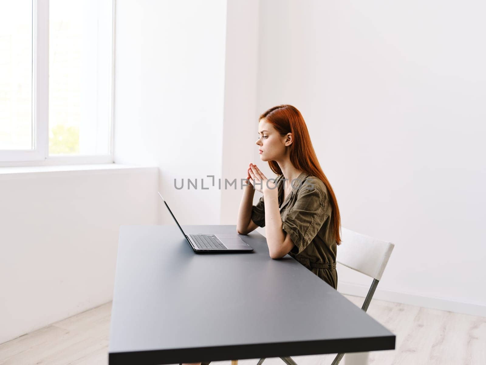 a slender, red-haired woman works at a laptop in a bright office room by Vichizh