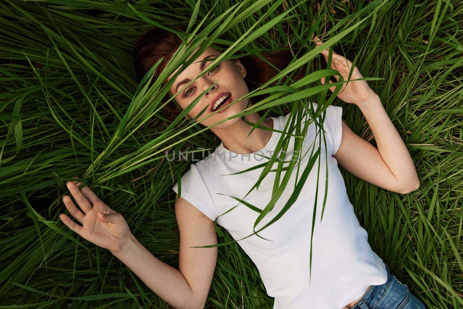 happy woman lies in high grass biting leaves with beautiful, even teeth by Vichizh
