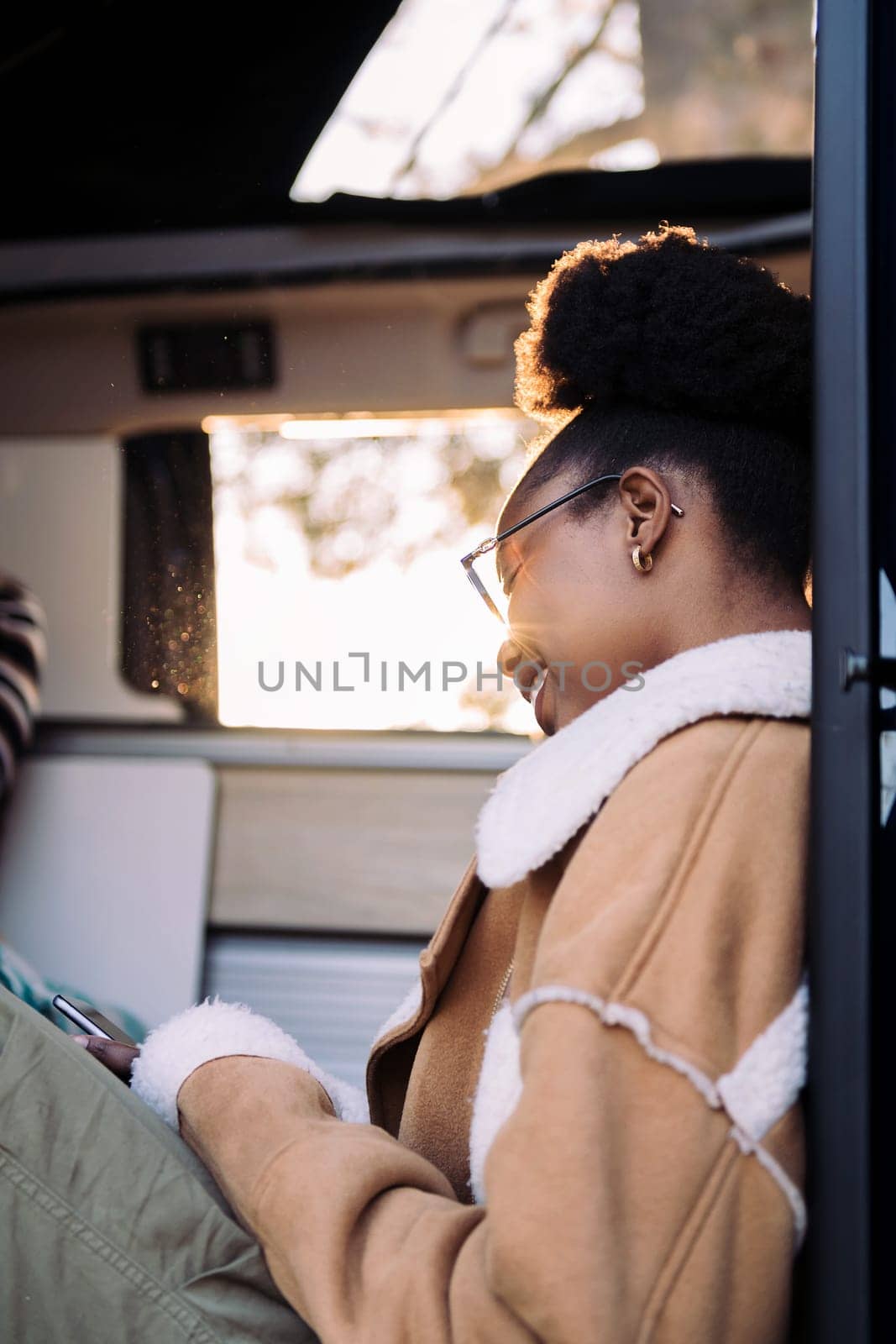 joyful black woman in camper van checking phone, concept of adventure travel and technology of communication