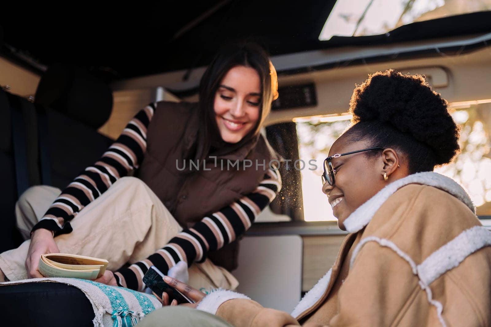 two young women chilling reading during a road trip in camper van, concept of travel and adventure with best friend