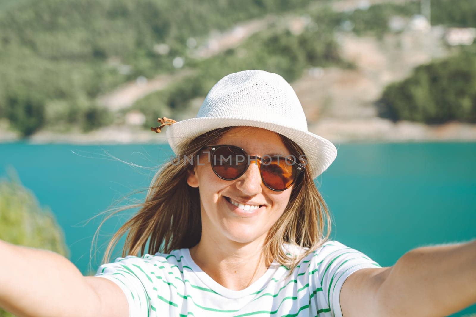 Woman taking selfie photo with wide angle front camera of mountains lake background. Traveler female having fun on the blue lake outdoors travel adventure vacation by Ostanina