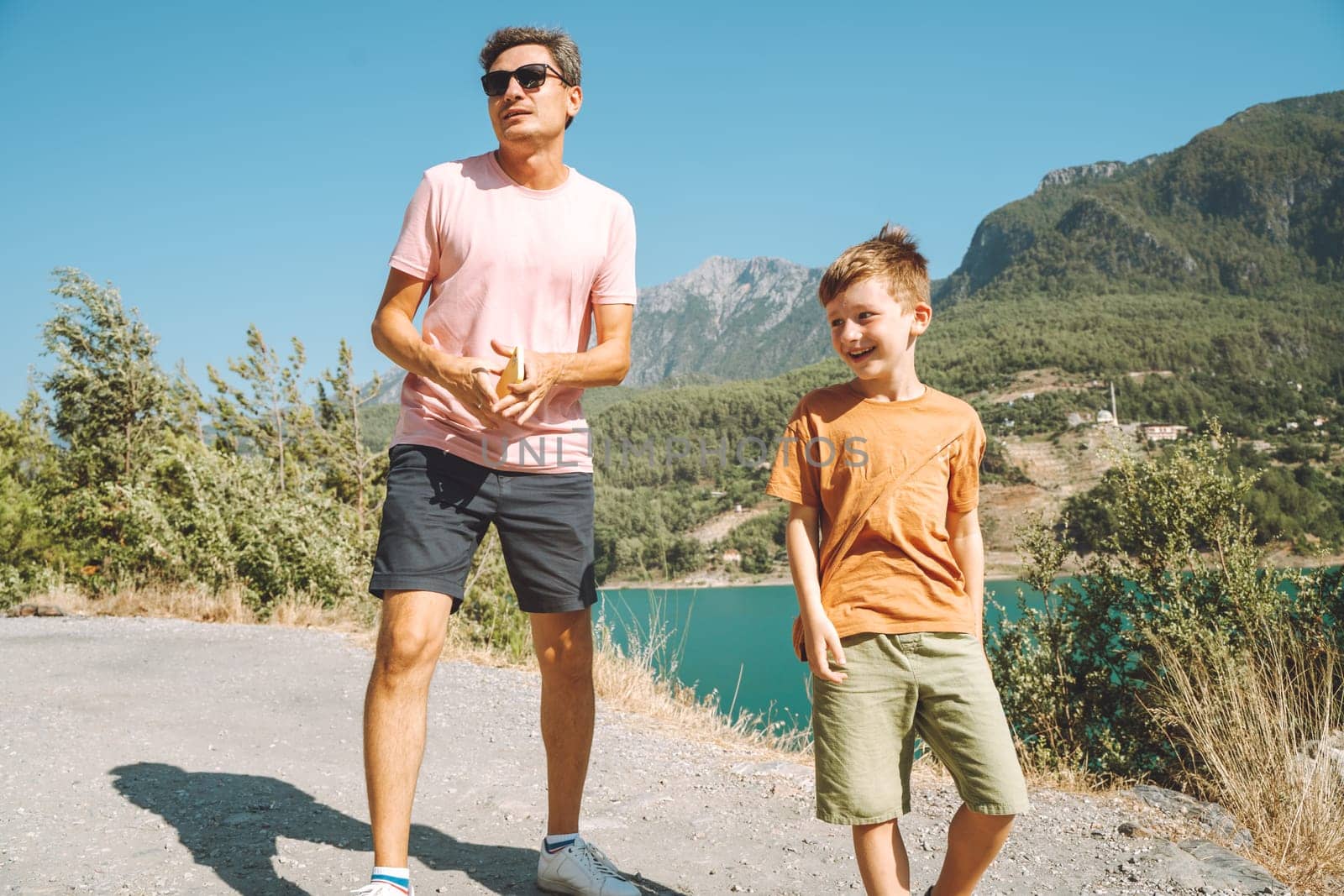 Young dad and his son standing on Mountain View. Child kid boy having fun with father and hiking hiking near mountains lake on background by Ostanina