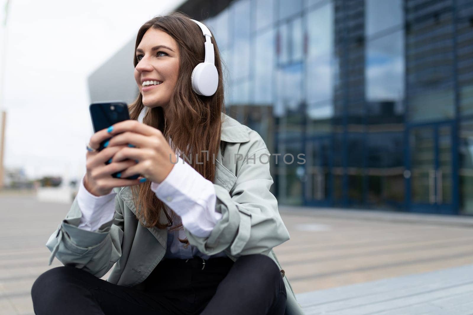 satisfied girl tourist resting sitting on the sidewalk of the street and listening to music in headphones by TRMK