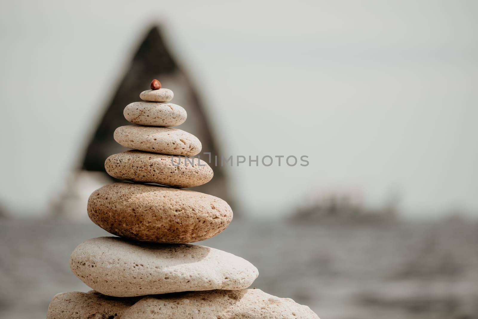 Balanced rock pyramid on sea pebbles beach, sunny day and clear sky at sunset. Golden sea bokeh on background. Selective focus, zen stones on sea beach, meditation, spa, harmony, calm, balance concept by panophotograph