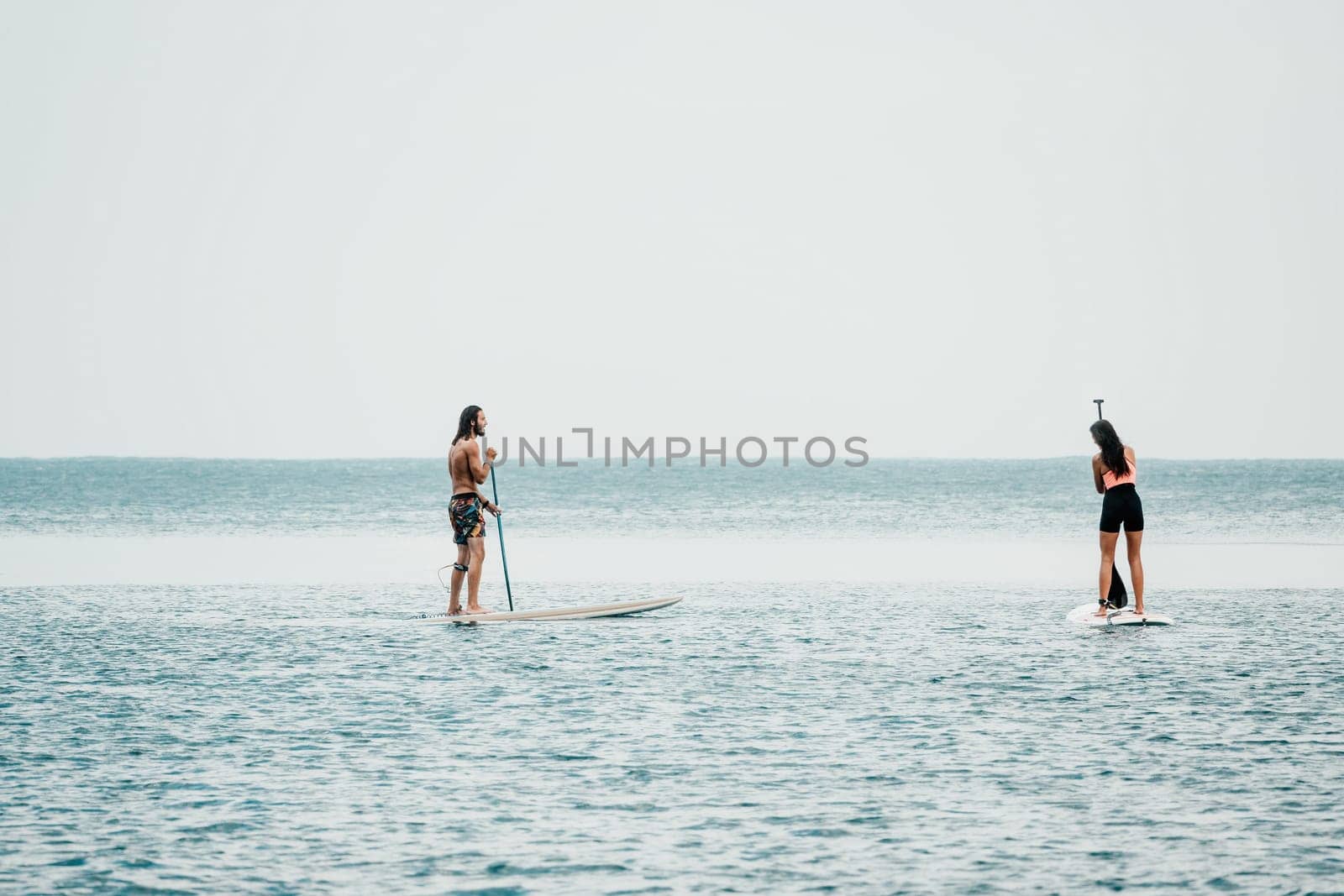 Sea woman and man on sup. Silhouette of happy young woman and man, surfing on SUP board, confident paddling through water surface. Idyllic sunset. Active lifestyle at sea or river