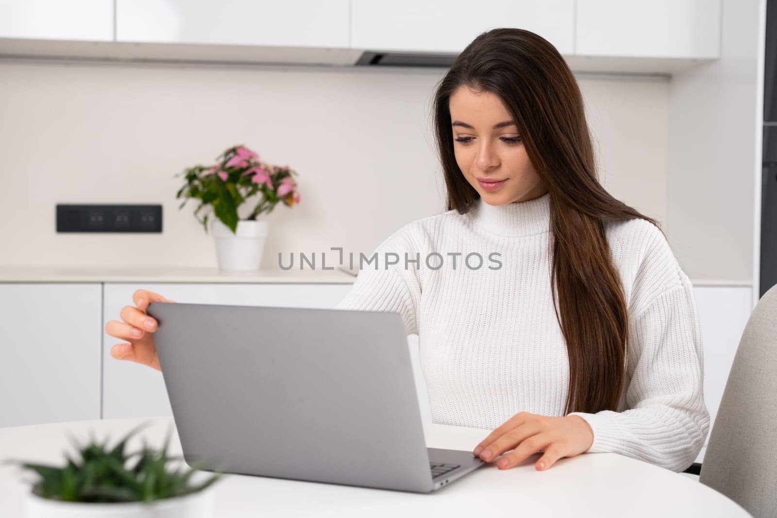 Young beautiful woman sits at her workplace and opens the laptop for working online. Freelance working at home.