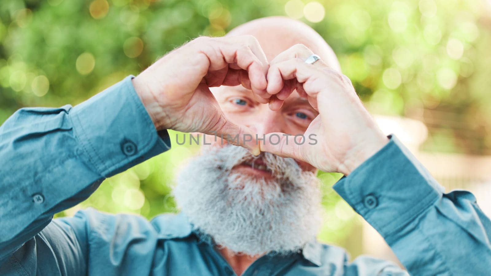 Portrait, hands and heart with a senior man outdoor in a garden during summer for love or health. Face, emoji and shape with a hand gesture by a mature male outside in a park for wellness or romance by YuriArcurs