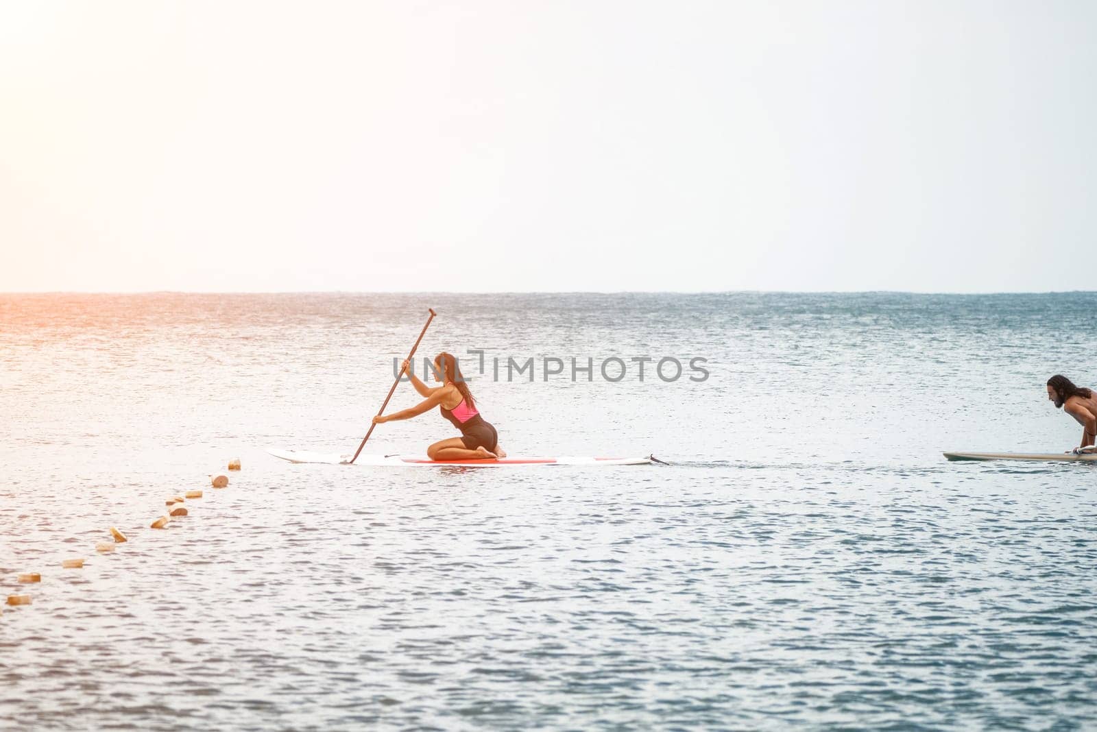 Sea woman and man on sup. Silhouette of happy young woman and man, surfing on SUP board, confident paddling through water surface. Idyllic sunset. Active lifestyle at sea or river