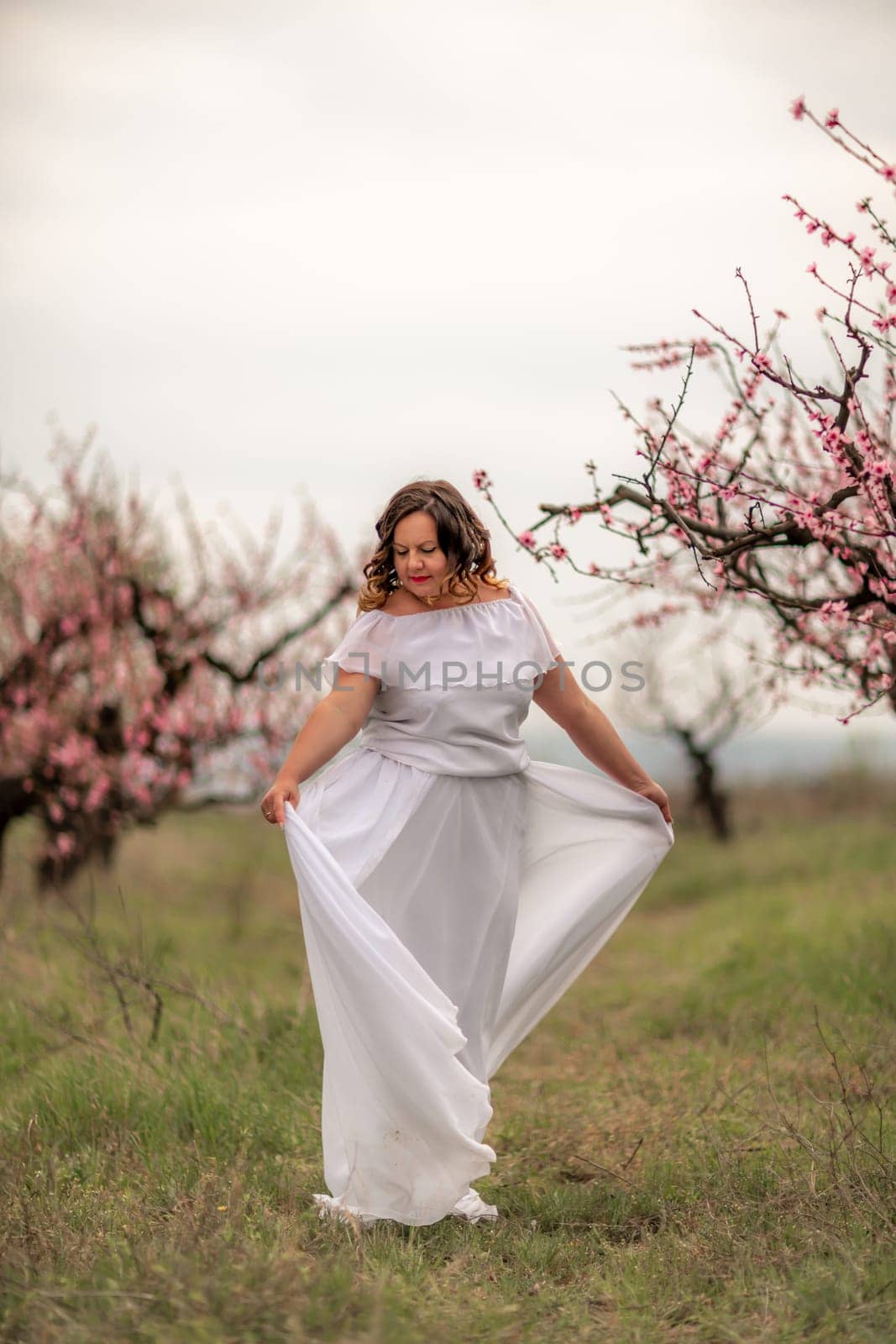 Woman peach blossom. Happy woman in white dress walking in the garden of blossoming peach trees in spring.