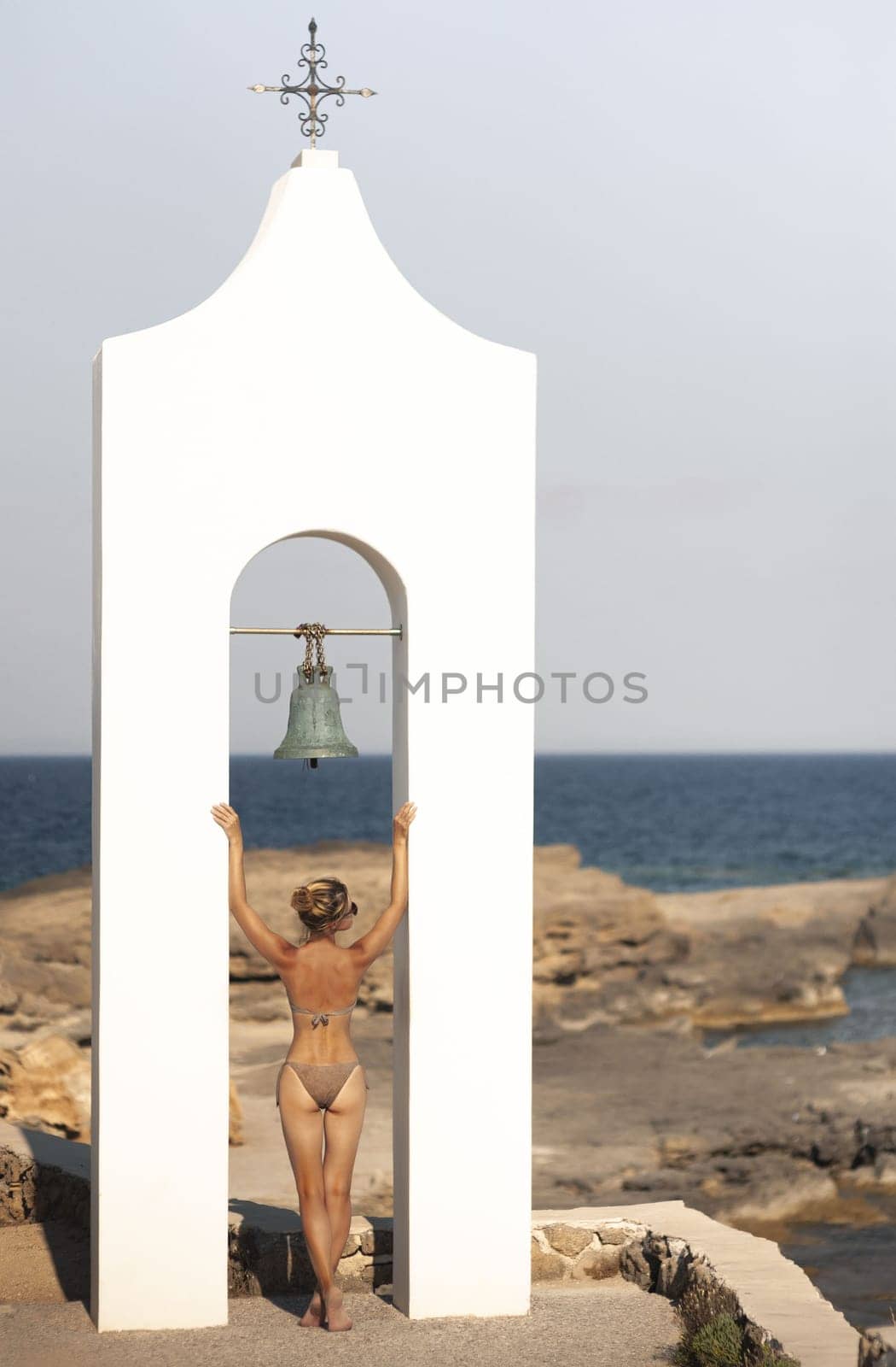 Young sexy woman posing on the beach in Greece. Woman sunbating with mediterranean sea at Santorini island greece. Young woman in a swimsuit on the background of Greek architecture and the sea. Woman in sexy bikini and santoini landscape. by Andrii_Ko