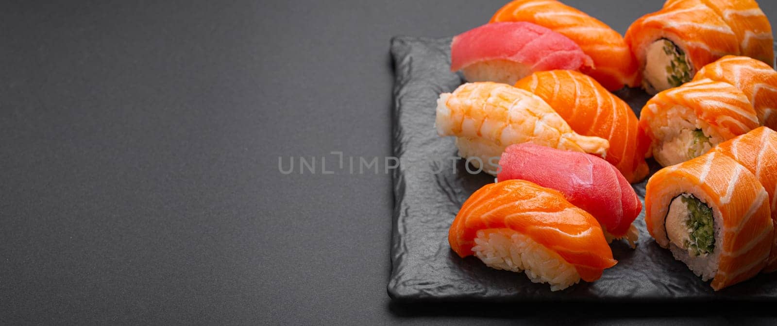 Set of traditional Japanese sushi and rolls angle view with soy sauce and wasabi on dark black rustic slate. Sushi with salmon, tuna, shrimp, space for text by its_al_dente