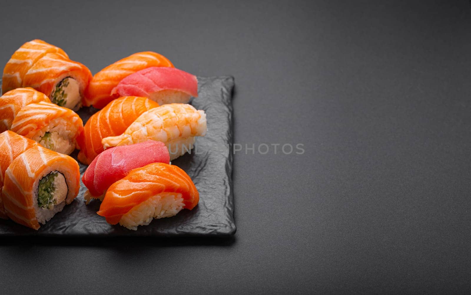 Set of traditional Japanese sushi and rolls angle view with soy sauce and wasabi on dark black rustic slate. Sushi with salmon, tuna and shrimp, space for text