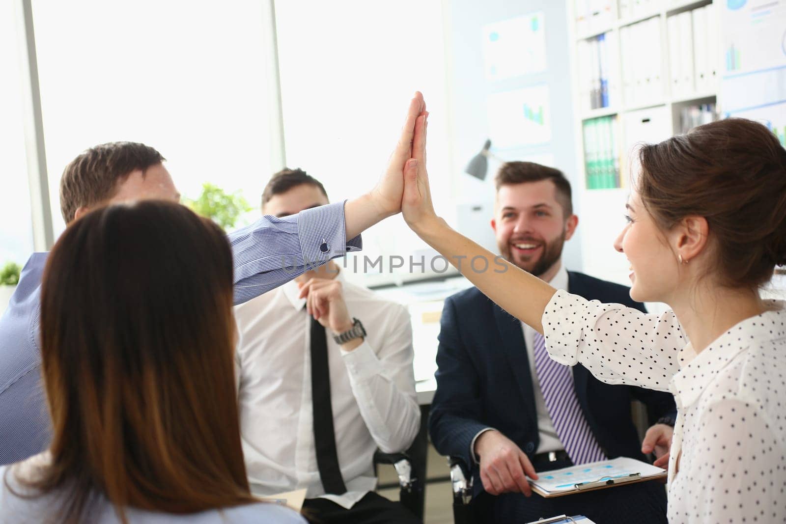 Enthusiastic teammates high-fives celebrate shared accomplishments and corporate success. Business people gathered at group meeting and team building concept