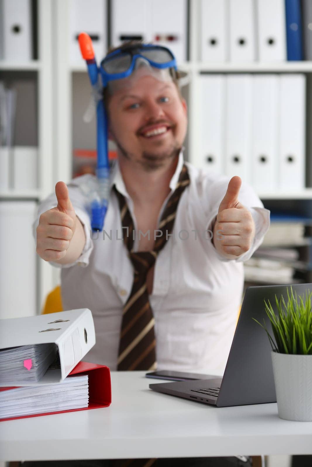 Man in swimming goggles shows OK gesture and holds thumbs up in office closeup by kuprevich