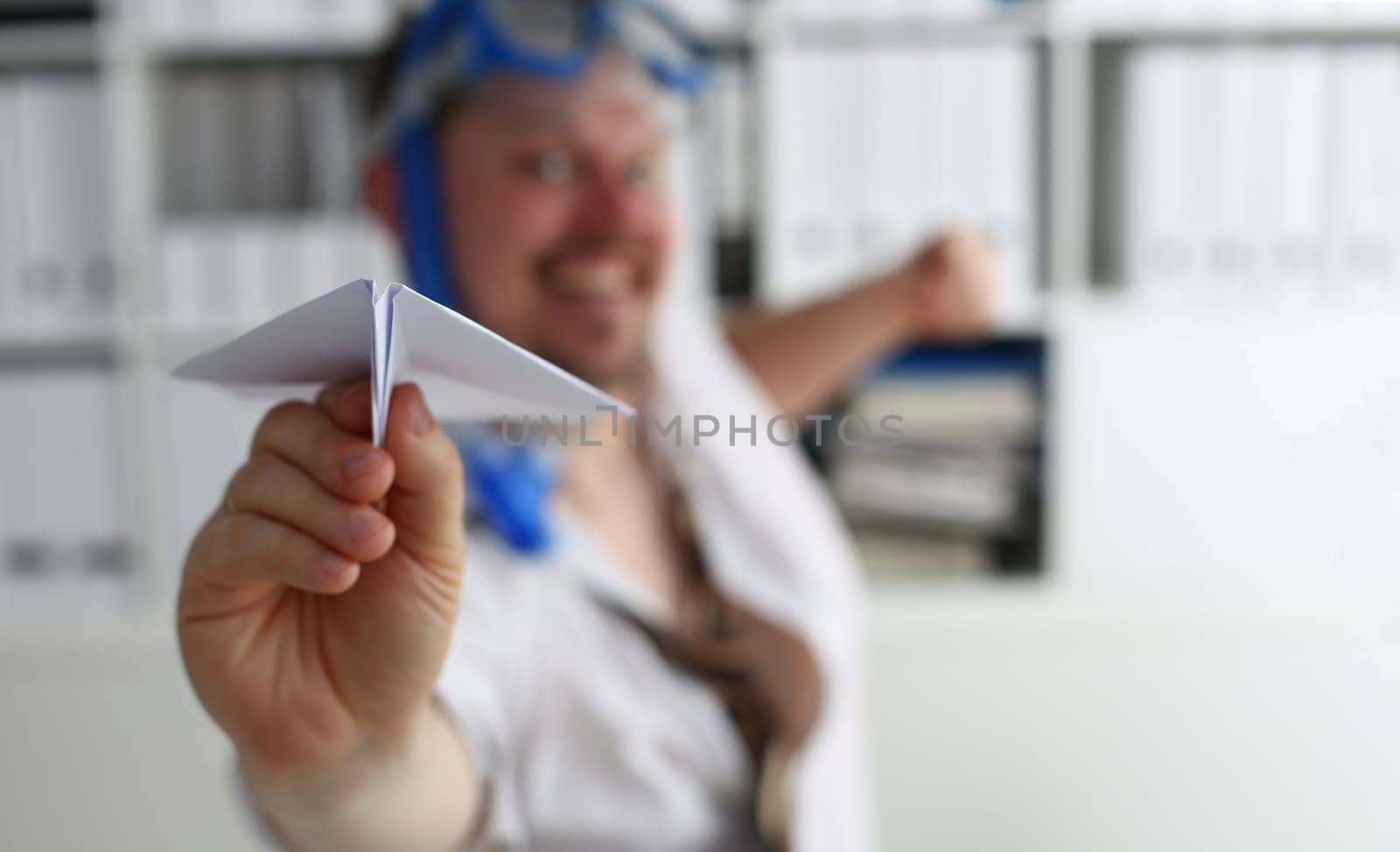 Man in swimming goggles plays and launches paper airplane in office. Booking air tickets for long-awaited vacation and traveling around world