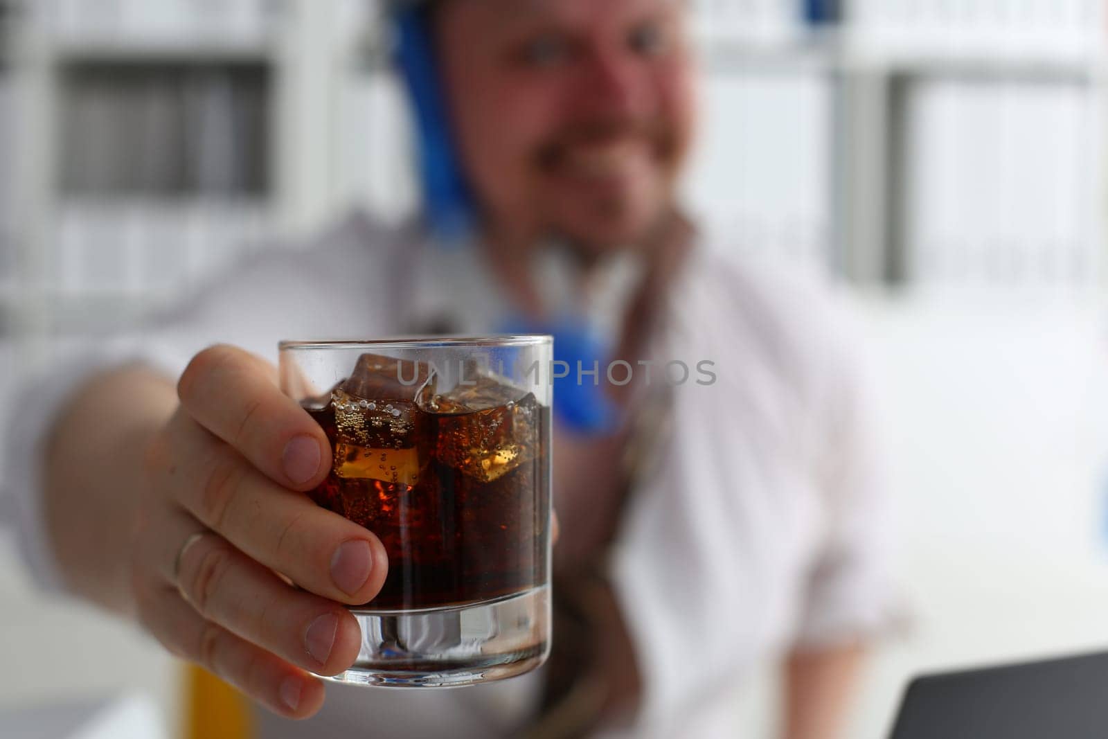 man holds a glass of cola and whiskey with ice in hand at workplace in office. Alcoholics and alcoholism in workplace