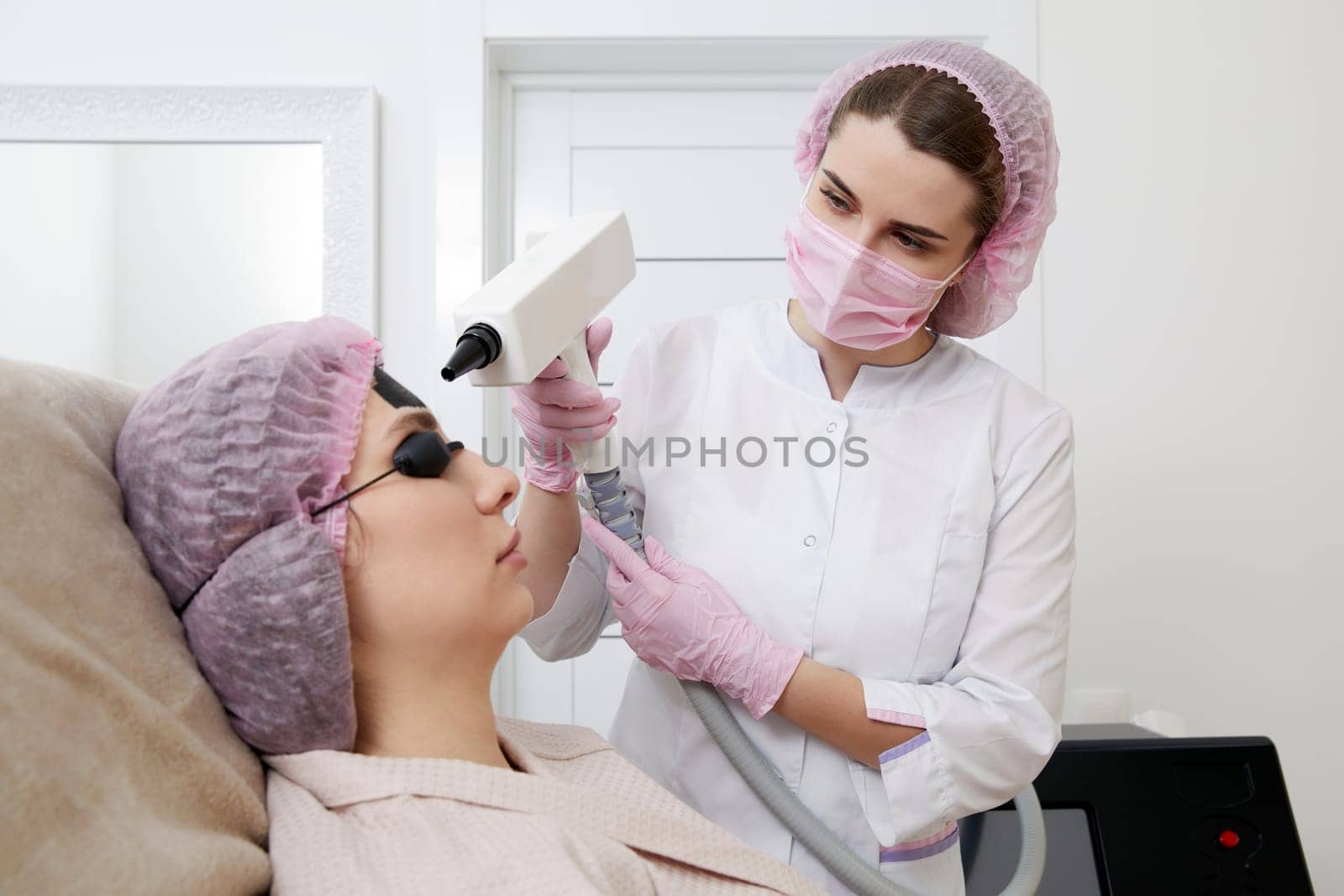Carbon peeling in beauty salon. Cosmetologist applying black mask on the face of beautiful woman for carbon peeling
