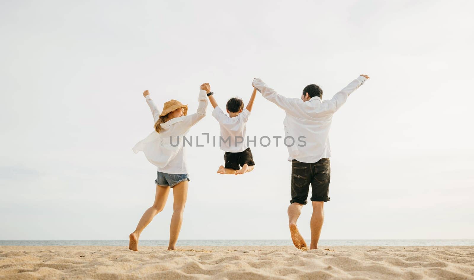 Back family mother, father and son holding hands and jumping in air at dawn time by Sorapop