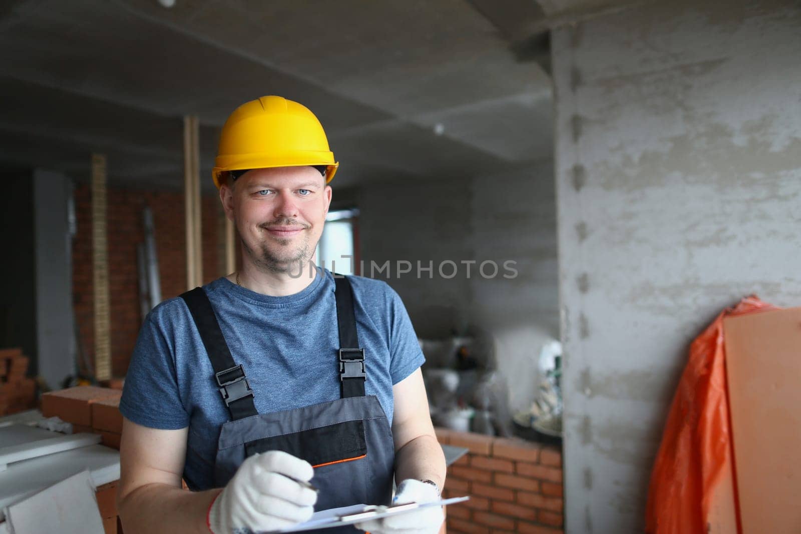 Smiling handsome male builder in hardhat holding pen and clipboard. Construction services and quality control of construction works
