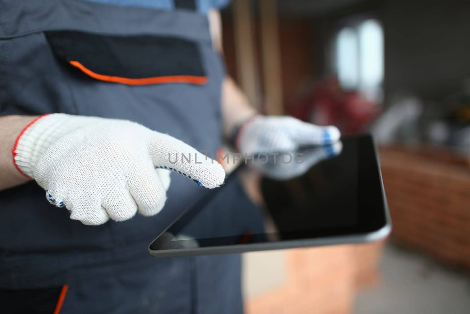 Builder hands in gloves use tablet for building and repairing premises. Applications and assistance in apartment renovation