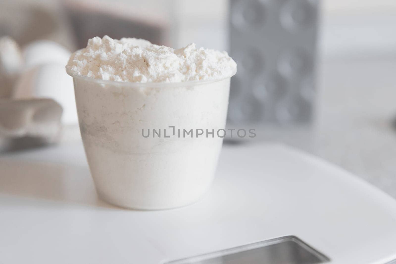 Close-up on measuring plastic cup with flour on a white kitchen scale, high key.