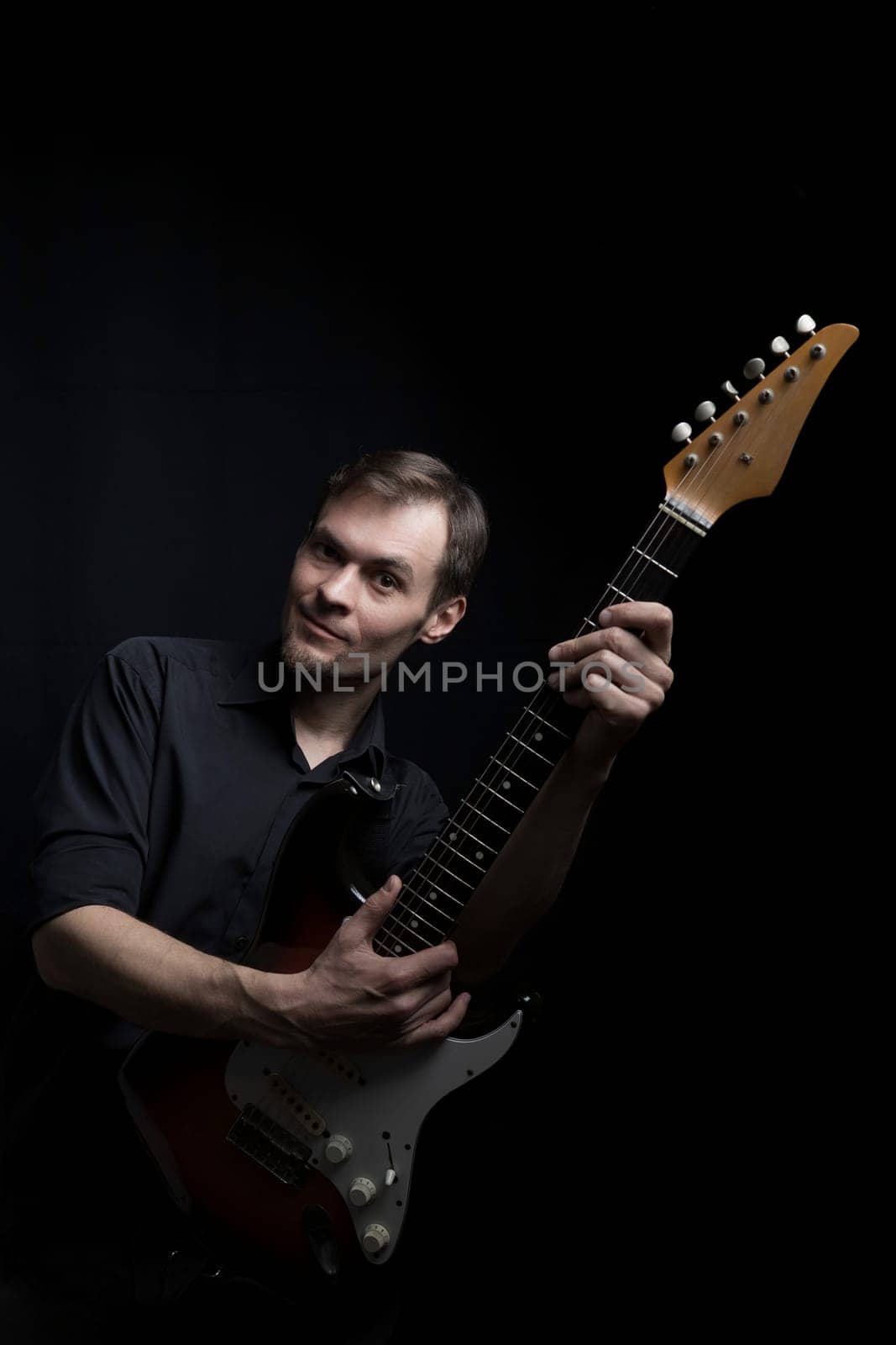 Caucasian man guitarist playing on electric guitar on black background.