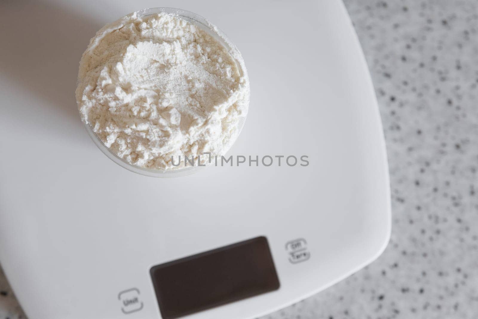 Top view on measuring cup with flour on a white kitchen scale.