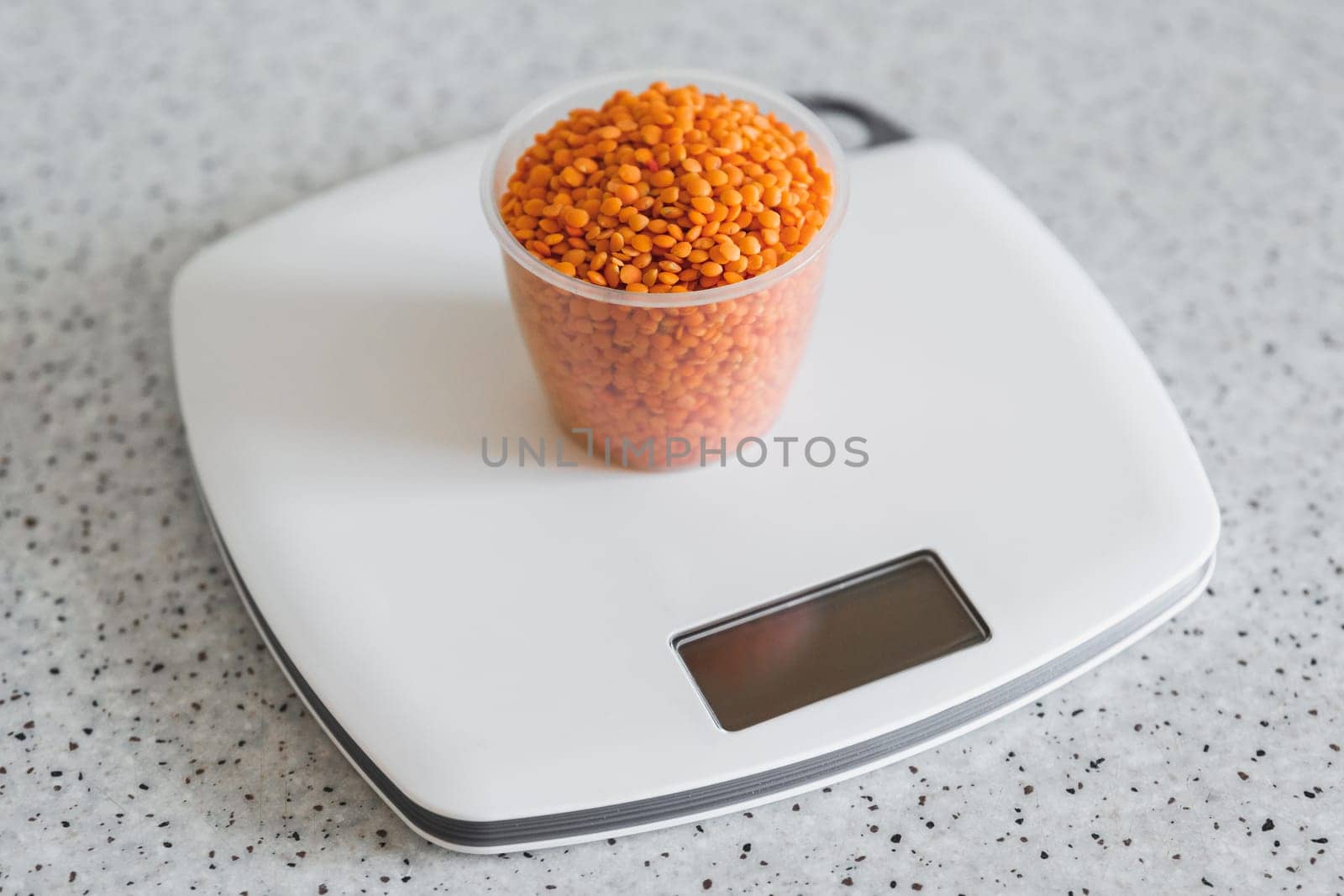 Lentils in a plastic measuring cup on an electronic kitchen scale.