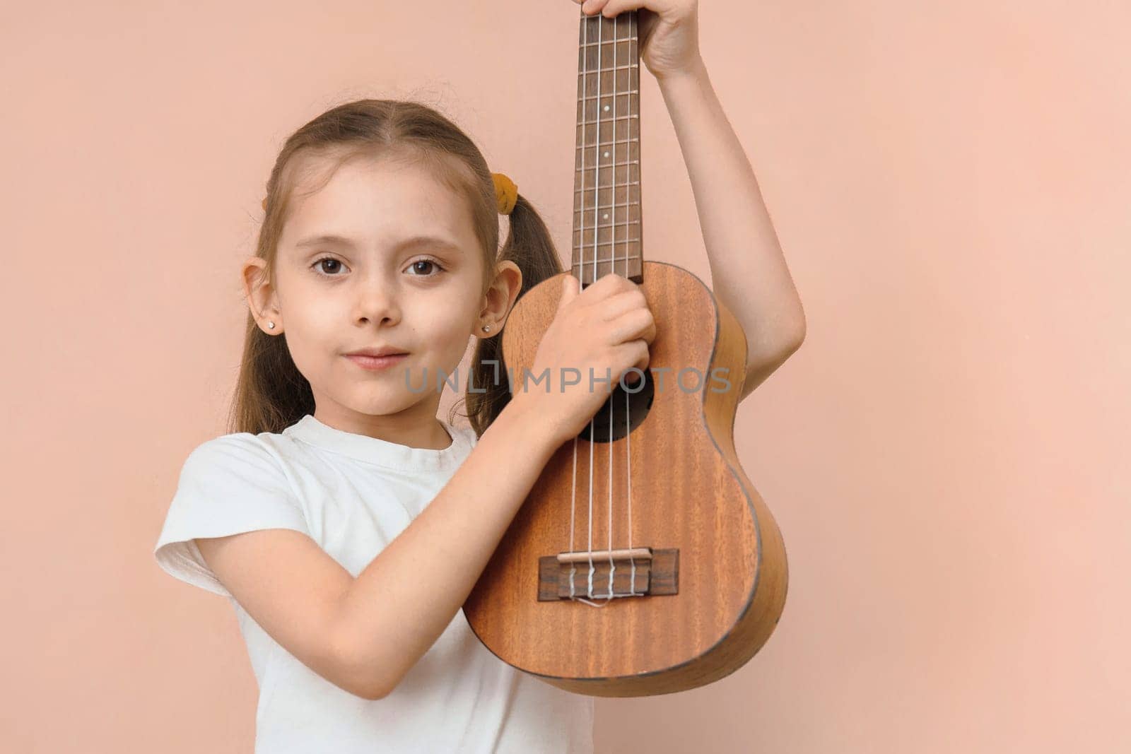 Caucasian preschool girl learns music by playing ukulele.