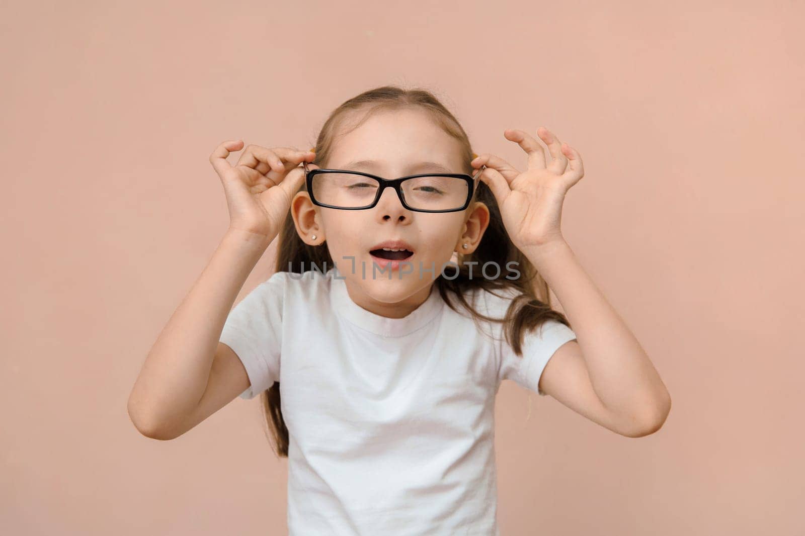 Portrait of a cute caucasian girl of elementary school age with poor eyesight wearing diopter glasses.